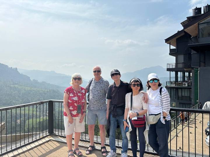 Small tour group poses at a scenic hilltop viewpoint overlooking lush green valleys in Sri Lanka.