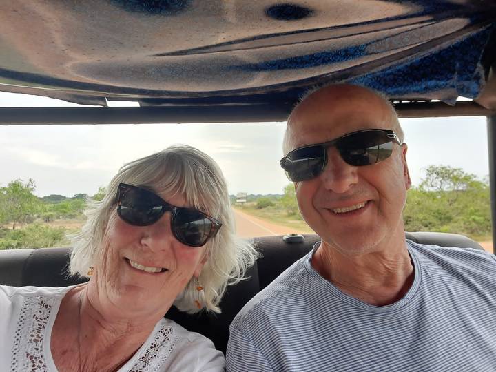 Close-up selfie of a couple wearing sunglasses during an open-top jeep ride.