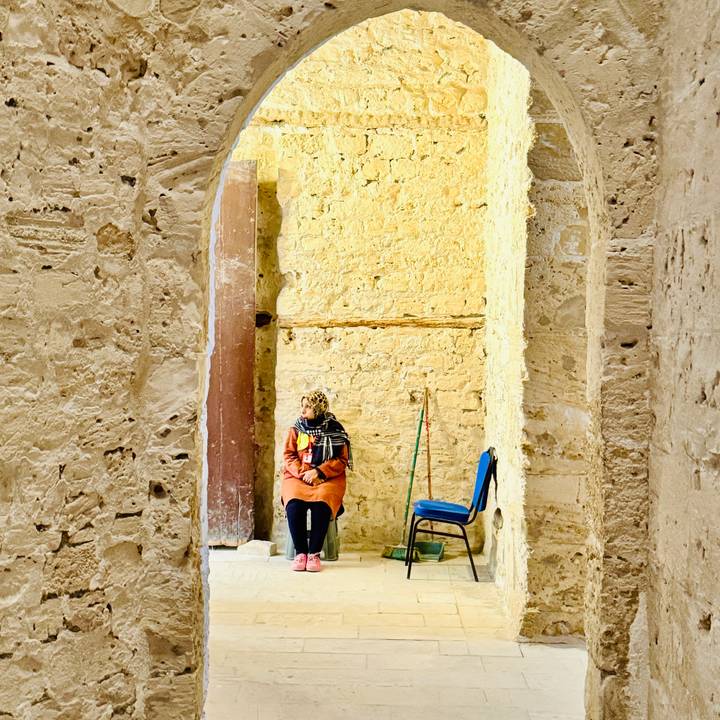 Visitor seated inside a sun-lit ancient temple corridor built of yellow stone.