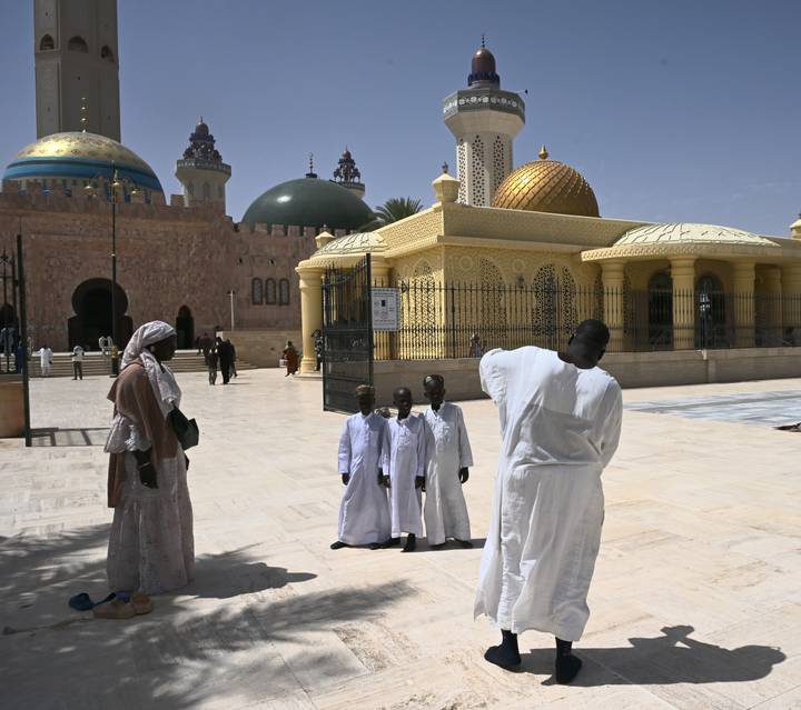 Visitors dressed in white pose for photos in the spacious courtyard of an ornate mosque with colorful domes.