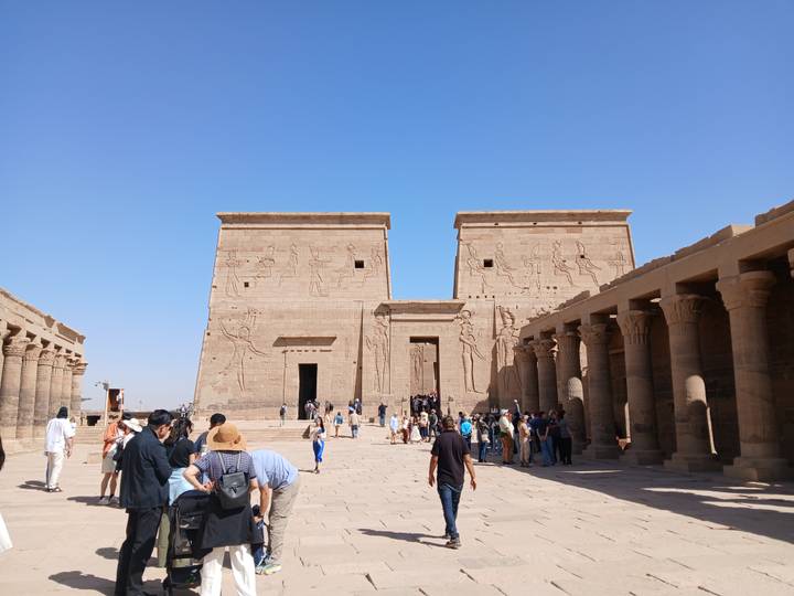 Crowds exploring the main courtyard of Philae Temple framed by colonnades and twin pylons.