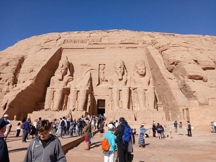 Iconic façade of Abu Simbel with throngs of visitors capturing photos beneath colossal statues.