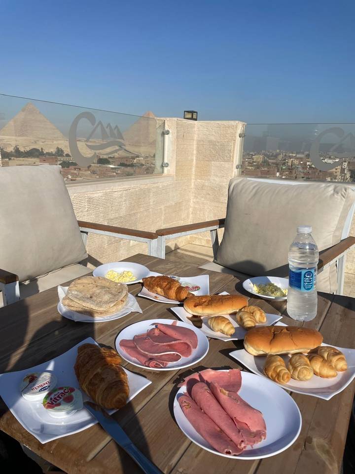 Outdoor breakfast table with pastries and city panorama, pyramids faintly visible in the hazy distance.