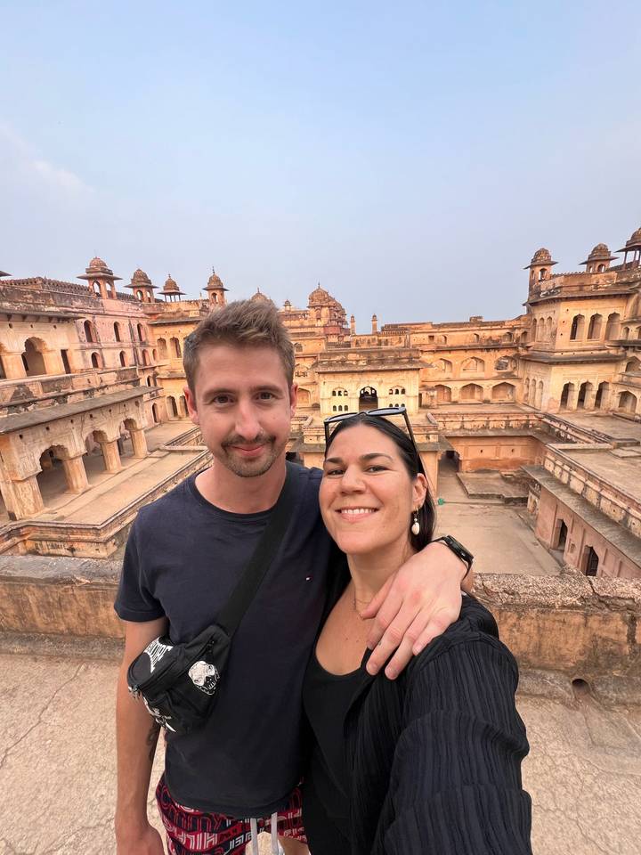 Smiling couple selfie on a terrace overlooking the ornate courtyards of a historic Indian palace.