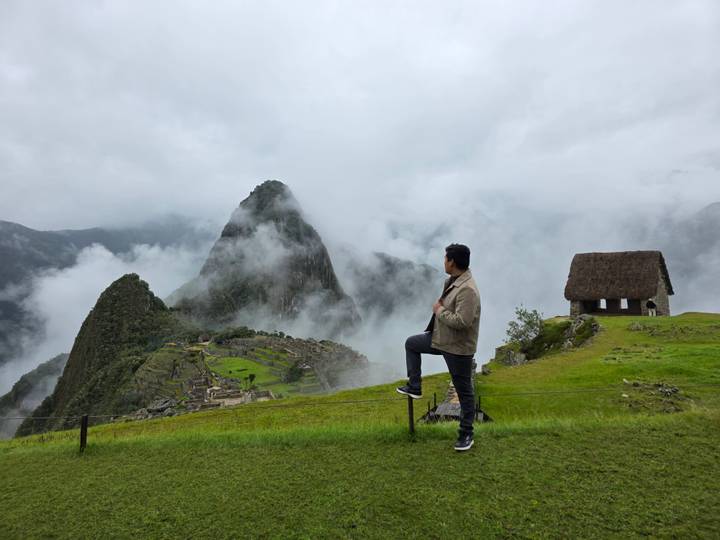 Traveler poses on a ridge overlooking cloud-kissed Machu Picchu ruins.