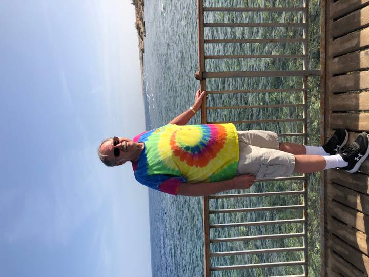 Traveler in tie-dye shirt standing on a wooden pier above clear Red Sea water.