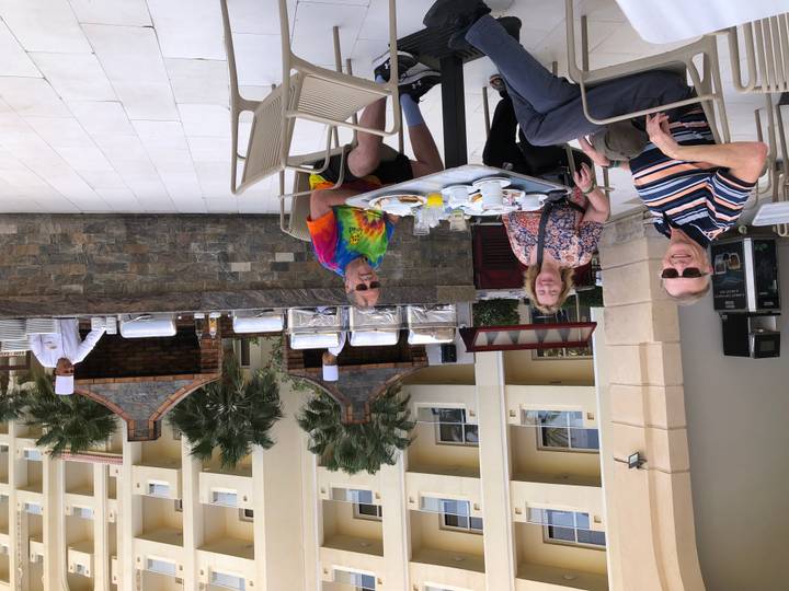 Friends enjoying breakfast on a resort terrace while chefs prepare food nearby.