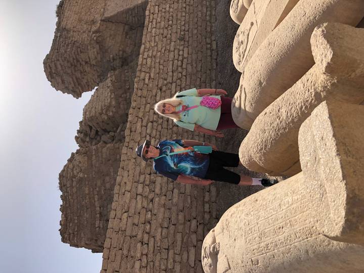 Two tourists stand among weather-worn stone ruins under a hazy desert sun.