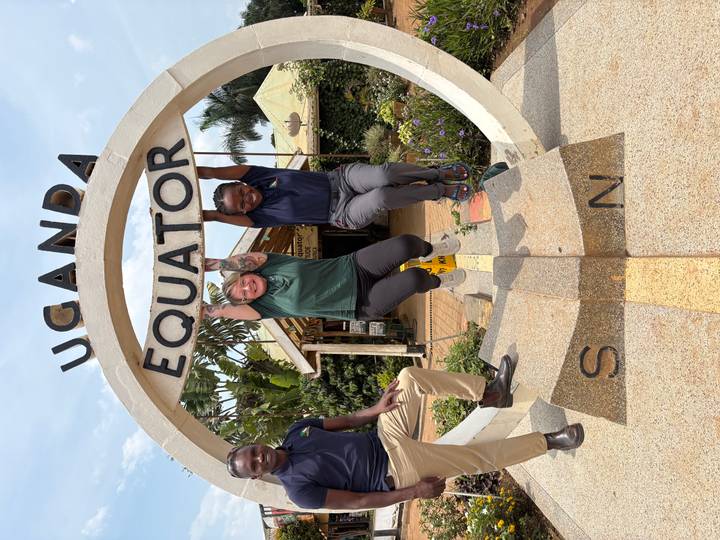 Travelers hang playfully from the Uganda Equator landmark arch for a photo.