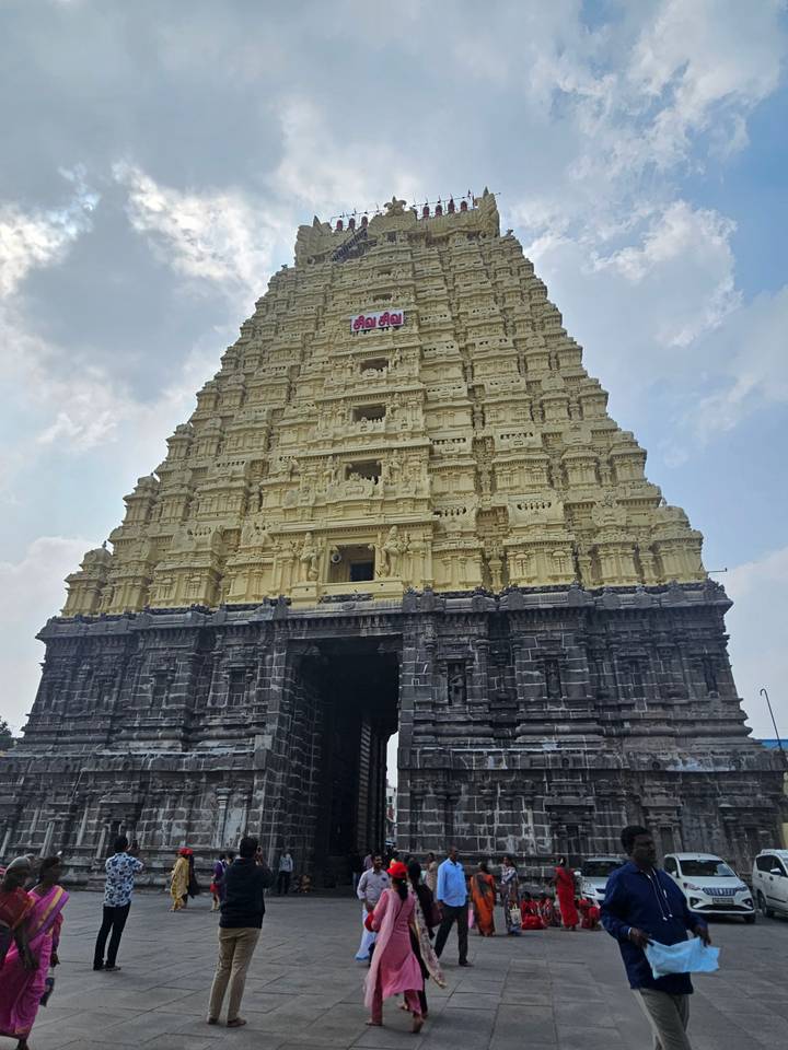 Front view of a tall yellow gopuram richly adorned with sculptures under blue sky.
