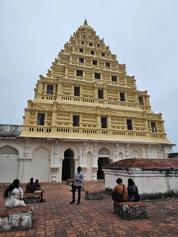 Close-up of an ornate pale-yellow South Indian temple gopuram with intricate carvings against a grey sky.