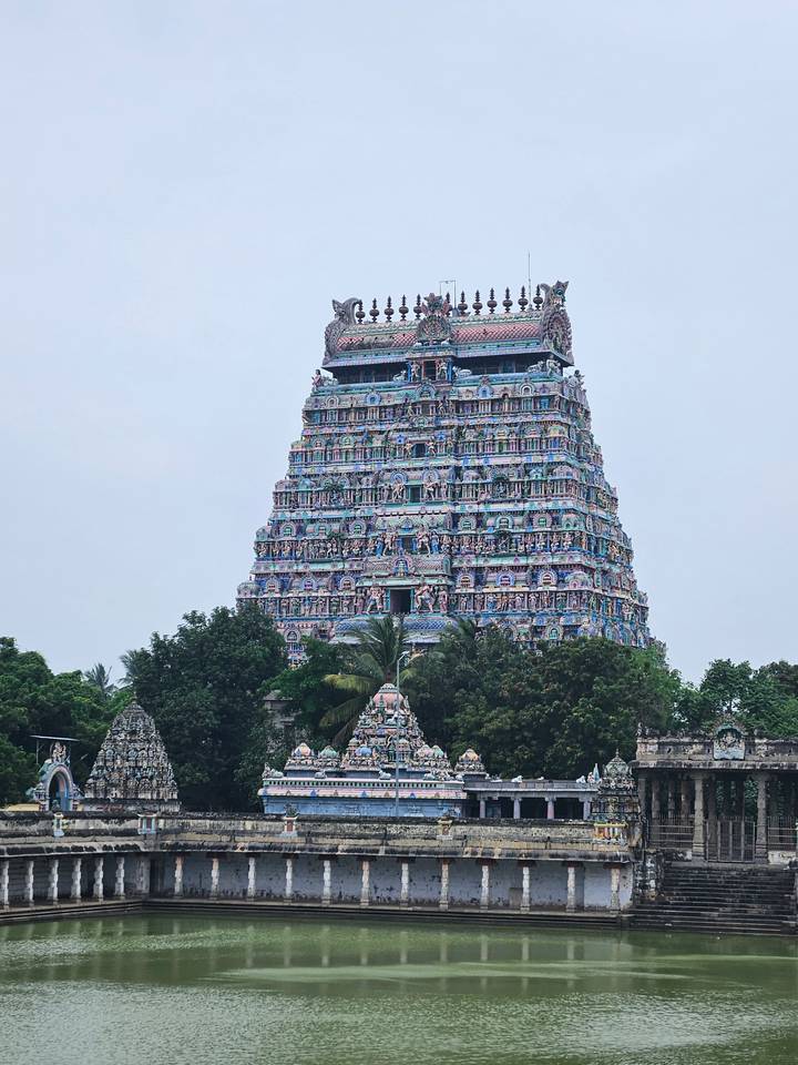 Vibrantly painted Sri Ranganathaswamy Temple gopuram soars above treetops under a pale sky.