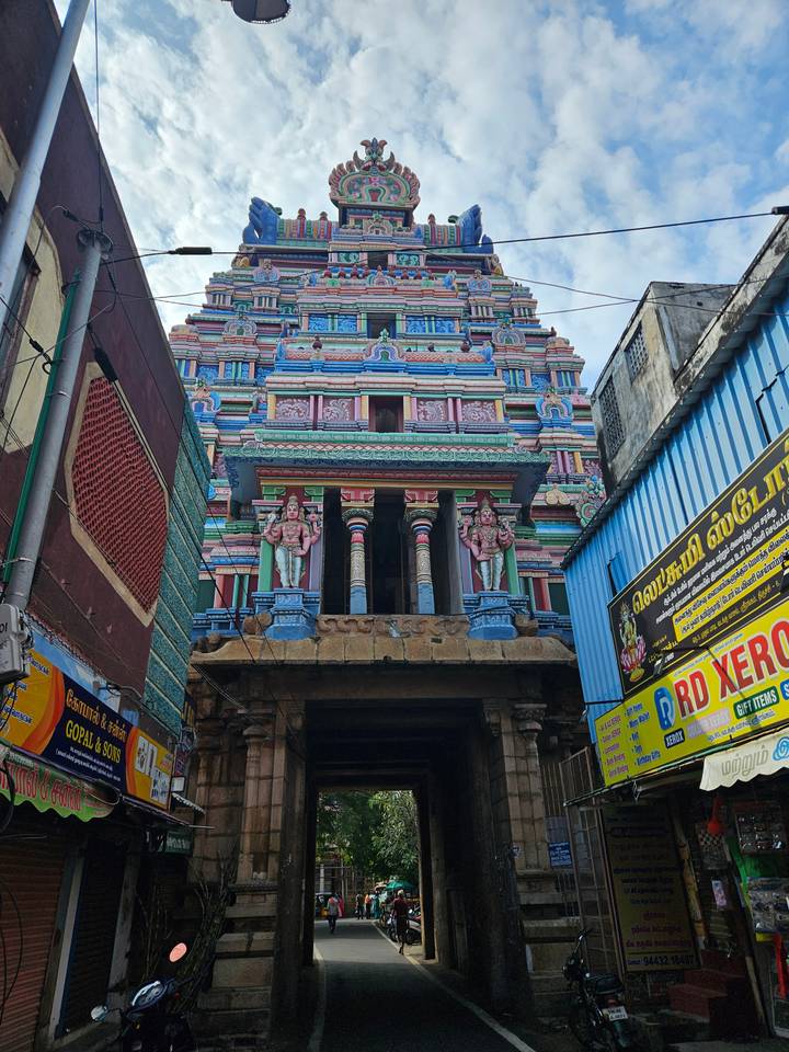 Street-level view of a colourful South Indian temple entrance nestled between urban buildings.