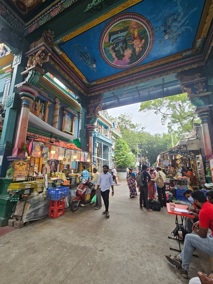 Bustling temple market arcade filled with colourful stalls, visitors and religious décor.