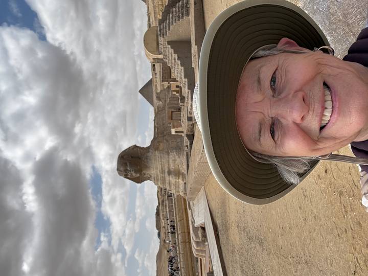 Smiling traveller selfie in front of the Great Sphinx with a pyramid and desert plateau beyond.