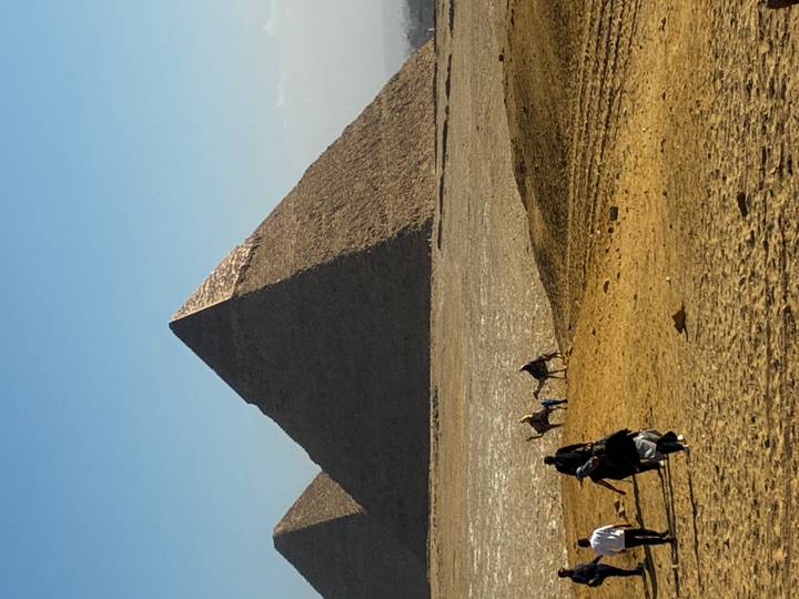Iconic pyramid rising above sandy desert as camel riders trek across the foreground.