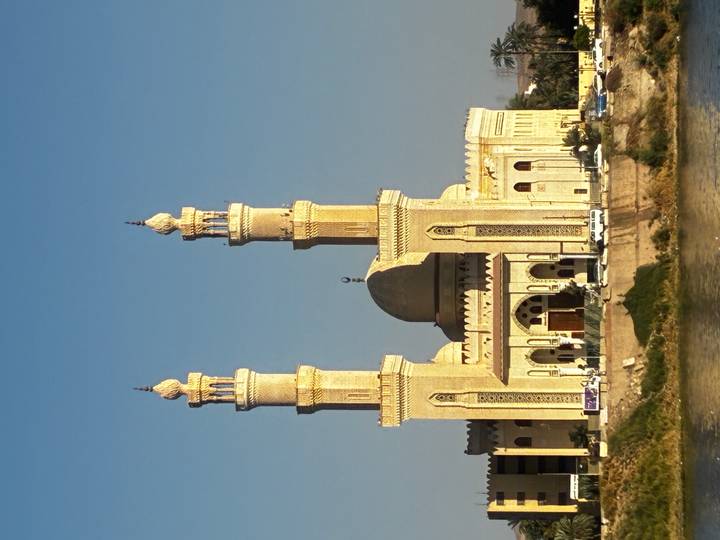 Elegant twin-minaret riverside mosque glowing golden in late afternoon light.