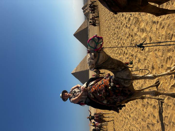 Rider atop a camel poses with the pyramids of Giza in the clear blue background.