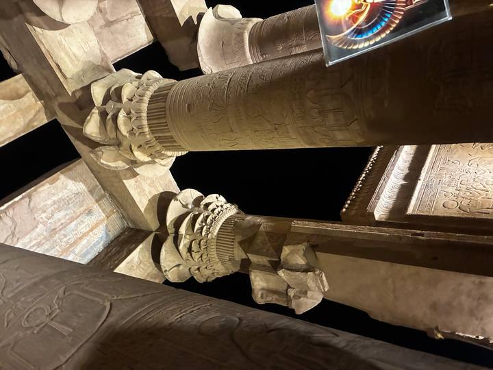 Night-lit hieroglyphic columns of an ancient Egyptian temple captured dramatically against black sky.