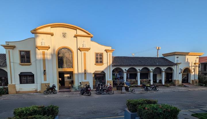 Long, low colonial building with arched portico and motorbikes parked out front in evening light.