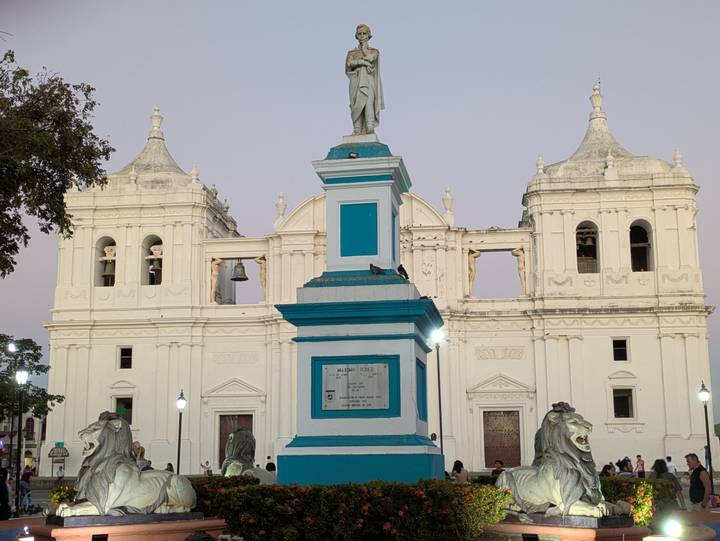 Front plaza of León Cathedral with turquoise monument base and white twin-towered church at dusk.