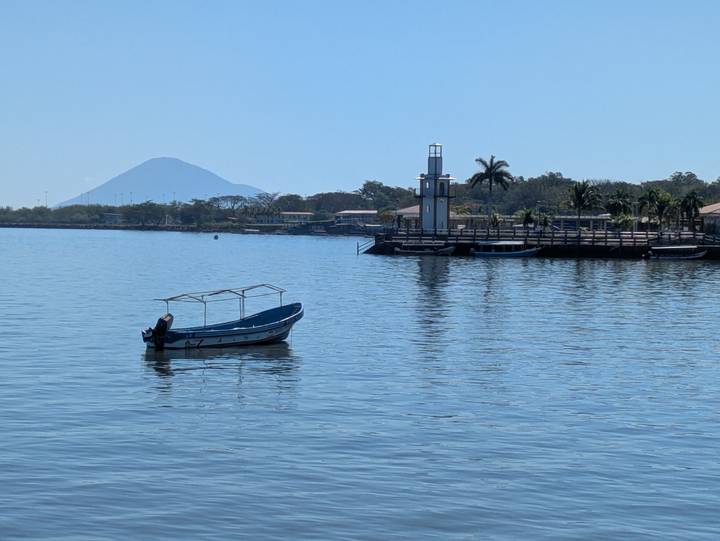 Small motorboat on a calm lake with lighthouse pier and a cone volcano in the distance.