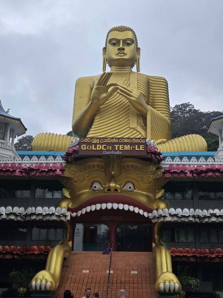 Giant golden Buddha statue above a wide-mouthed demon facade at the Golden Temple, Dambulla.