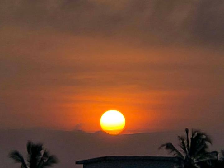 Fiery orange sun setting through hazy clouds creating a dramatic sky gradient.