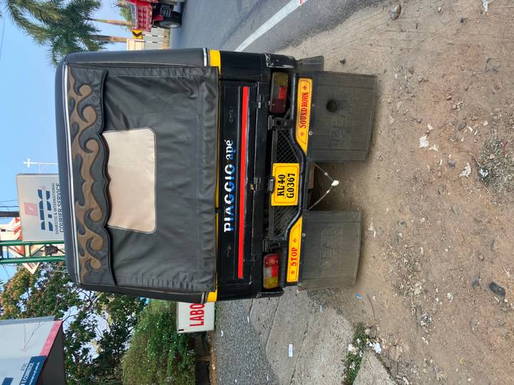 Rear view of a black auto-rickshaw with yellow license plate parked on a dusty roadside.
