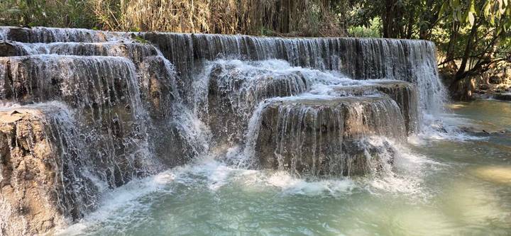 Turquoise water cascades over tiered limestone falls surrounded by lush foliage.