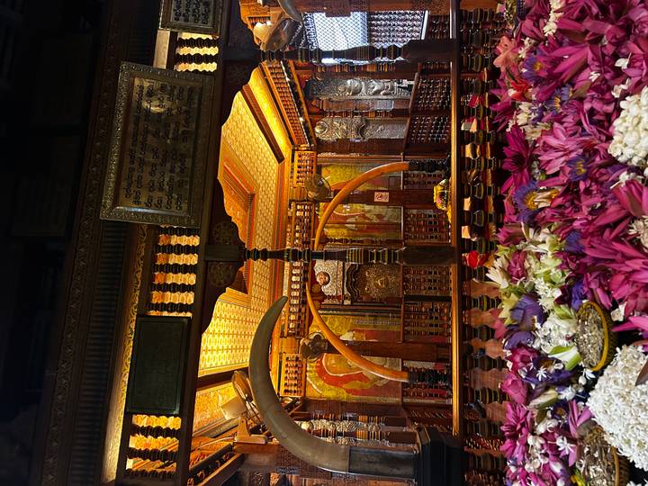 An ornate temple interior glows with golden light and vibrant flower offerings.