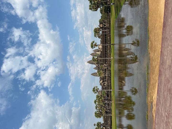 Iconic Angkor Wat temple reflected in still moat under partly cloudy skies.