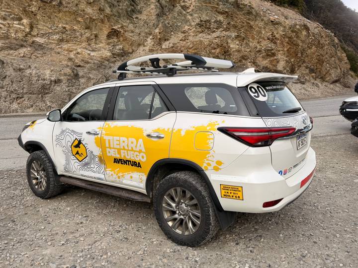 Off-road SUV branded 'Tierra del Fuego Aventura' parked on gravel roadside in rugged landscape.