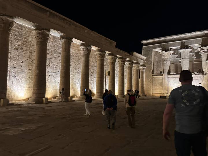 Night-time view of illuminated ancient Egyptian courtyard with tall carved columns and visitors exploring.