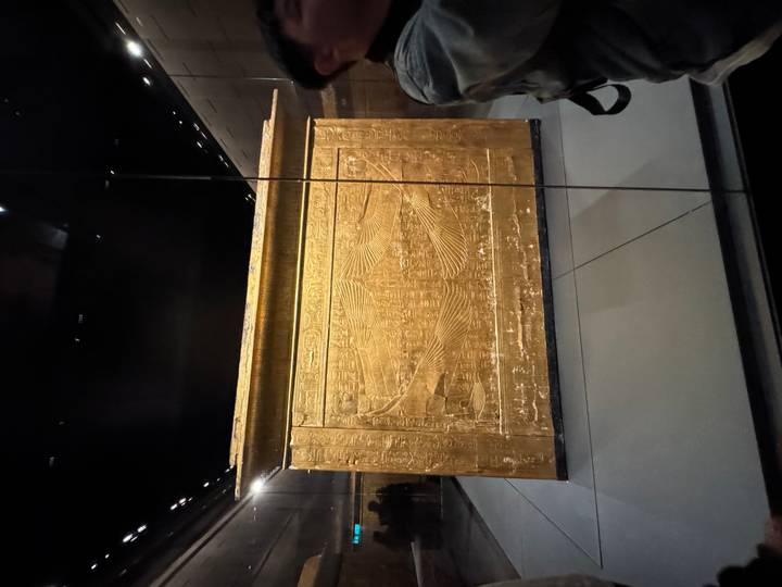 Golden inlaid shrine or sarcophagus displayed behind glass in a museum gallery.