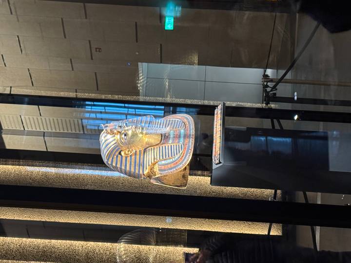 Golden funerary mask of an Egyptian pharaoh displayed in a glass showcase.