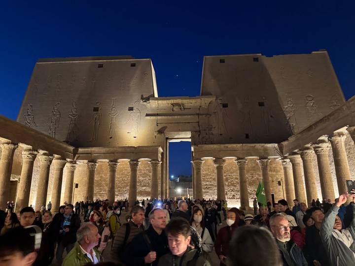 Crowd gathered in the illuminated forecourt of an ancient Egyptian temple at night.