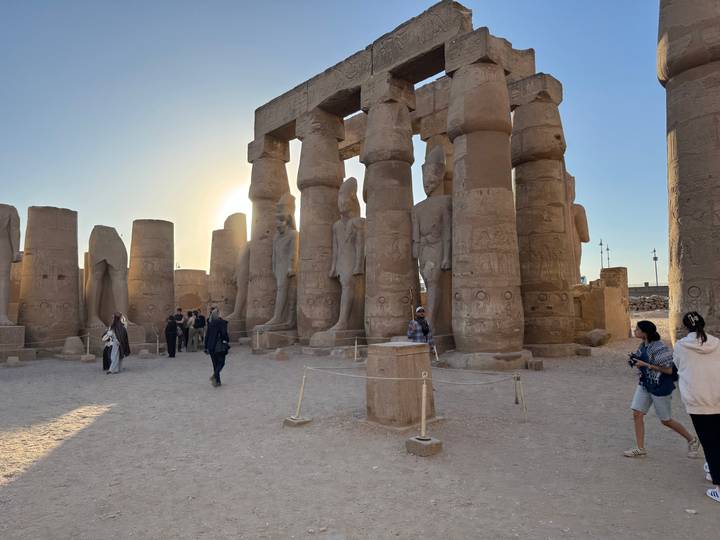 Sunset light silhouettes colossal statues and columns at Luxor Temple with visitors exploring.