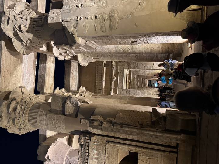 Night-time procession of tourists through towering, carved columns lit by warm spotlights.
