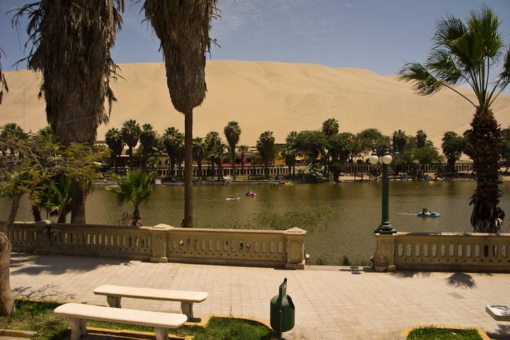 Desert oasis of Huacachina with palm-lined lagoon, sand dunes and kayakers enjoying the water.