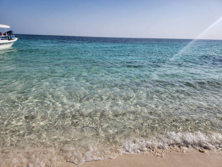 Crystal-clear turquoise sea with small boat at left on a sunny day.