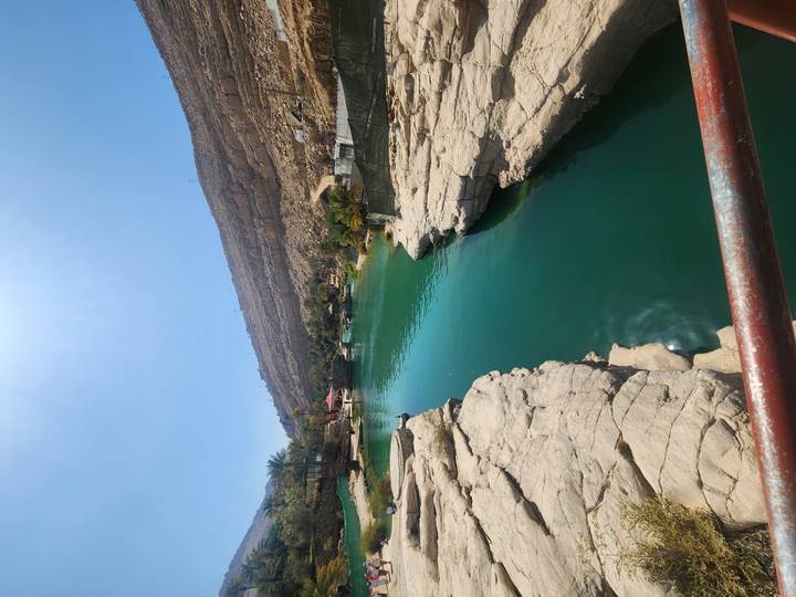 Emerald natural pool winding through rocky canyon with arid hillsides in bright sunlight.