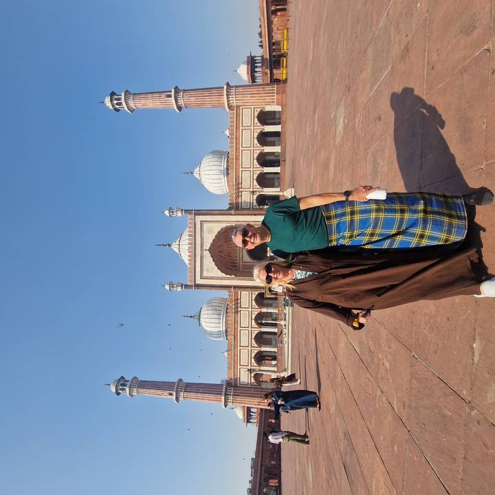 Two tourists stand in front of the grand Jama Masjid courtyard on a clear day.