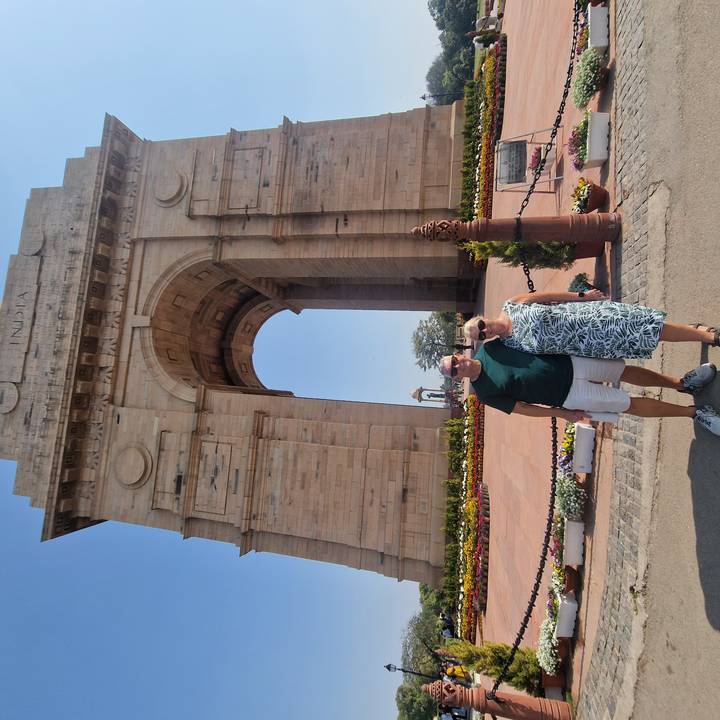Couple standing beneath the towering stone arch of India Gate surrounded by colourful flower beds.
