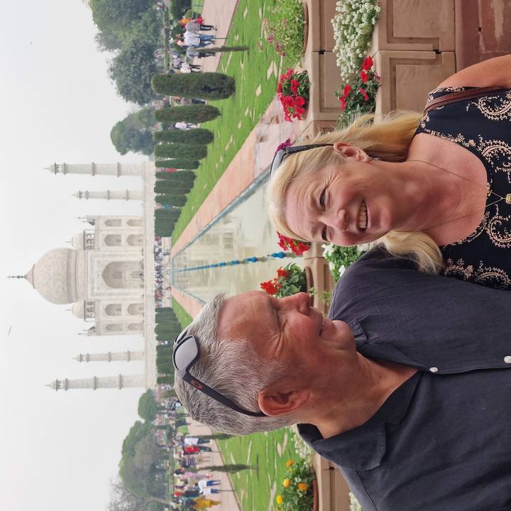 Couple smiling at each other with the Taj Mahal and its reflecting pool in the background.