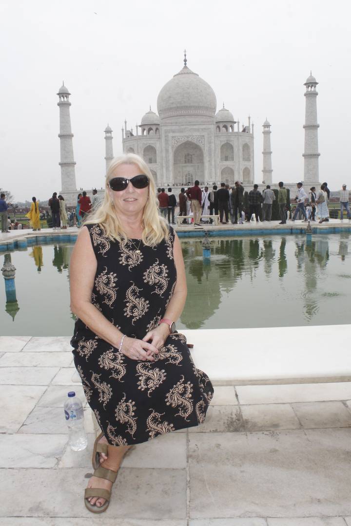 Female traveller sitting by the green reflecting pool in front of the Taj Mahal with crowds behind her.