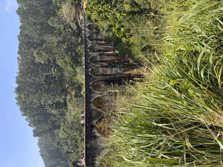 Iconic Nine Arches Bridge spanning a lush valley with tourists walking atop the stone arches.