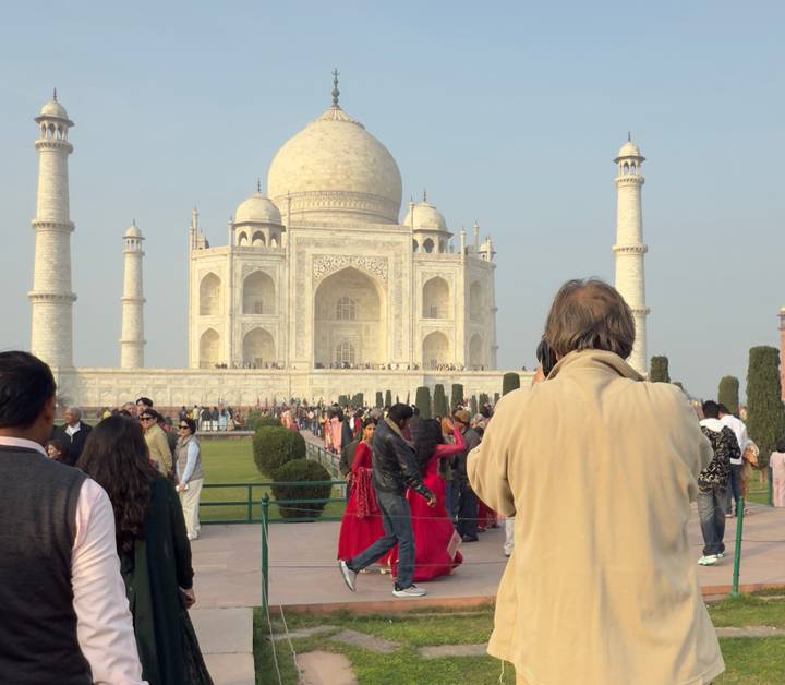 Crowds gather in front of the white marble Taj Mahal while a photographer captures the scene.