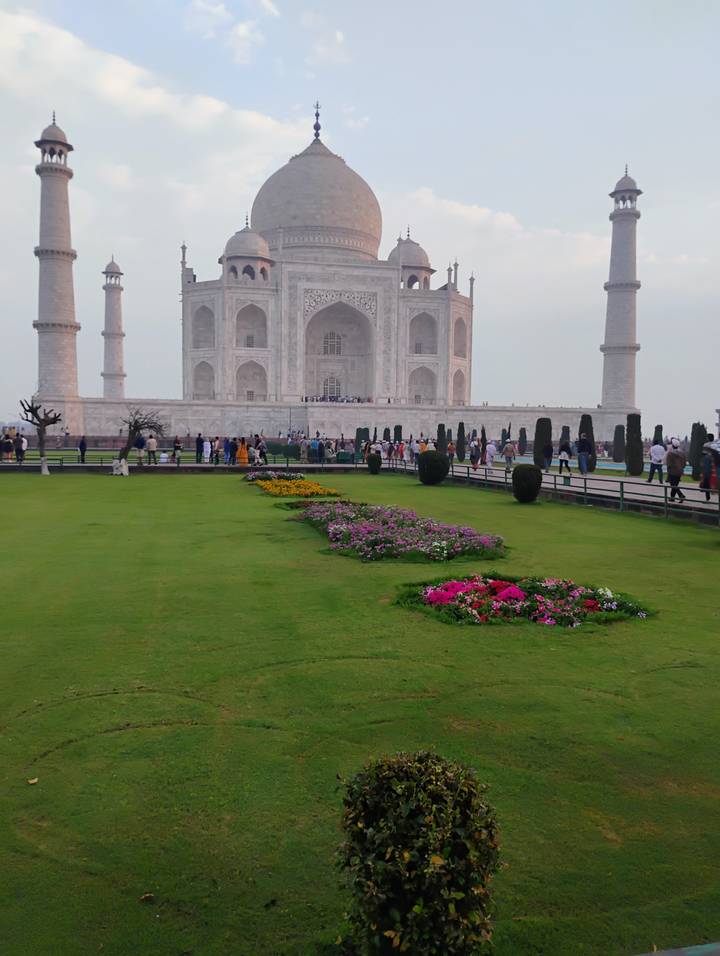 Lush lawns and colorful flowerbeds lead to the Taj Mahal as crowds gather along its marble plinth.