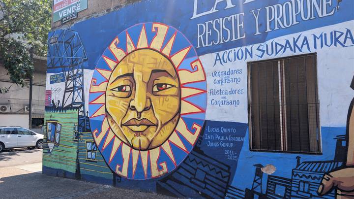 Vibrant street mural featuring a stylized sun face and Spanish slogans on a blue wall in La Boca.
